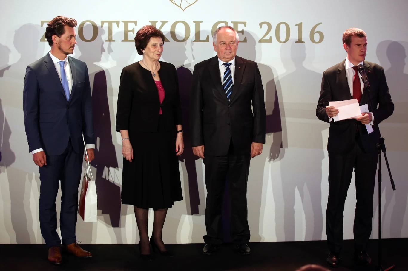 Dariusz Trafas (pierwszy od lewej) w 2016 roku Cztery osoby w eleganckich strojach stoją na scenie podczas oficjalnej gali, jedna z nich trzyma kopertę i przemawia do mikrofonu, a w tle widoczny jest napis ZŁOTE KOŁCE 2016.