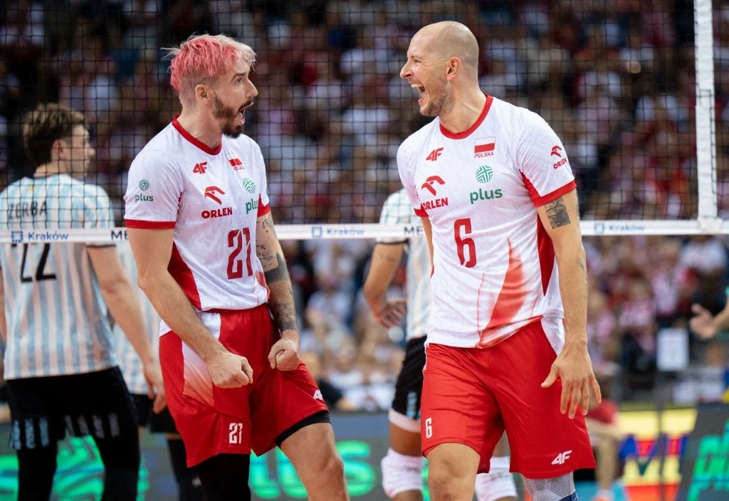 Tomasz Fornal wypowiedział się na temat Bartosza Kurka Dwóch siatkarzy w biało-czerwonych strojach drużyny narodowej Polski świętujących zdobycie punktu na boisku, wokół nich widać innych zawodników i kibiców na trybunach.