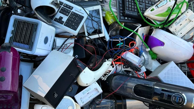 Stos różnorodnych zużytych sprzętów elektronicznych, takich jak klawiatury, czajniki, odkurzacze, ładowarki, przewody i inne małe urządzenia, ułożonych chaotycznie w jednym miejscu.