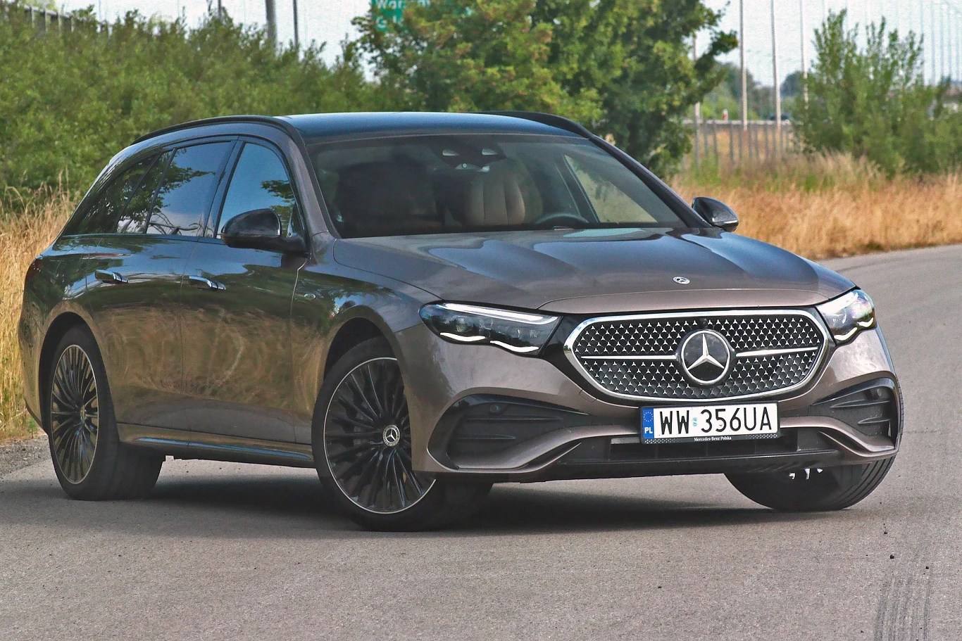 Luksusowy samochód osobowy marki Mercedes-Benz, model kombi w szarym kolorze, stoi zaparkowany na ulicy z widocznym czarnym grillem, charakterystycznym logo producenta oraz polską tablicą rejestracyjną.