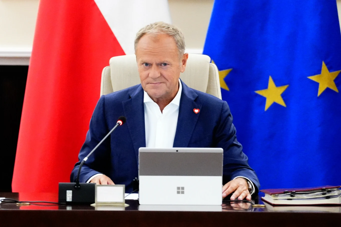 Większość Polaków nie wierzy, że Donald Tusk zrealizuje obietnice wyborcze Mężczyzna w garniturze siedzi przy stole konferencyjnym, korzystając z laptopa, w tle widoczne flagi Polski oraz Unii Europejskiej.