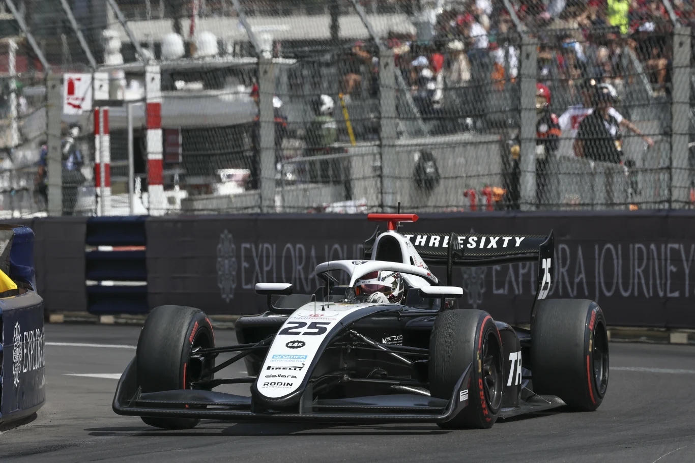 Bolid wyścigowy F2 z numerem 25 pokonuje zakręt na torze ulicznym podczas zawodów, za siatką widoczna jest publiczność oraz elementy infrastruktury wyścigowej.