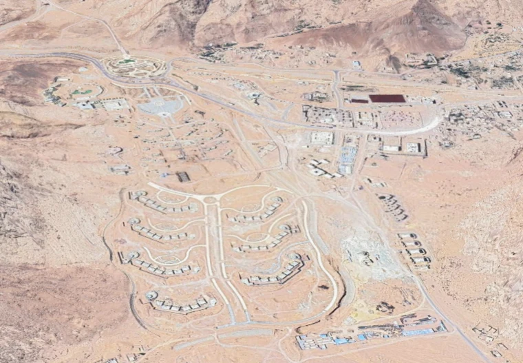 Osiedle domów jednorodzinnych na pustynnym, pagórkowatym terenie z wyraźnie zaznaczonym układem ulic oraz rozproszoną infrastrukturą i pojedynczymi zabudowaniami w tle.