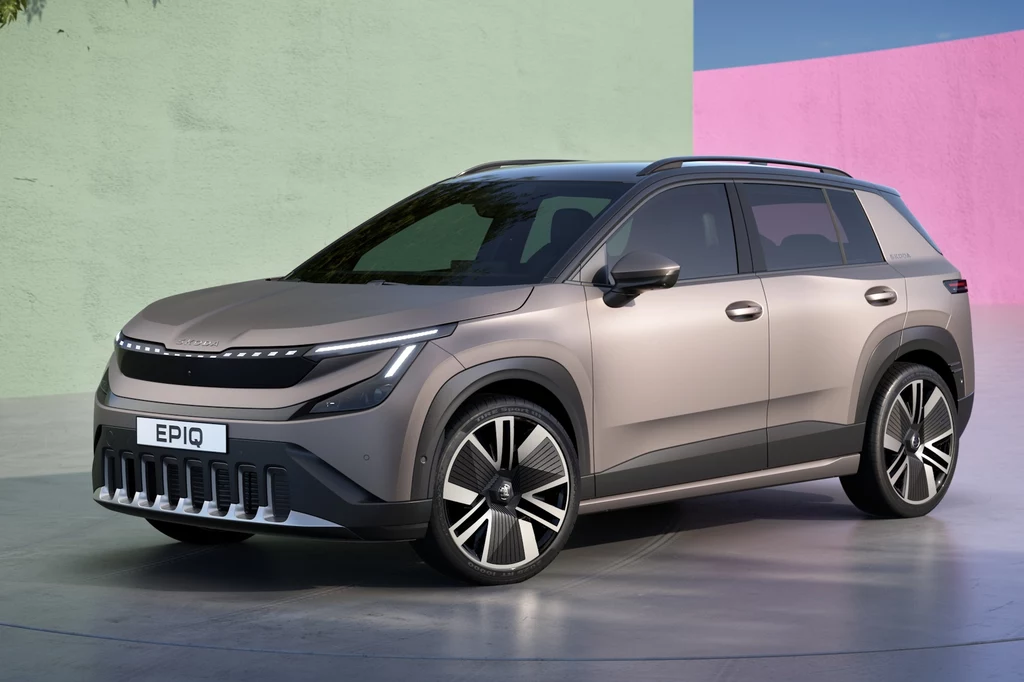 Skoda Epiq Nowoczesny SUV w kolorze szarym zaparkowany na tle pastelowej ściany, z wyraźnie widocznymi czarnymi felgami oraz futurystycznym designem reflektorów i grilla.