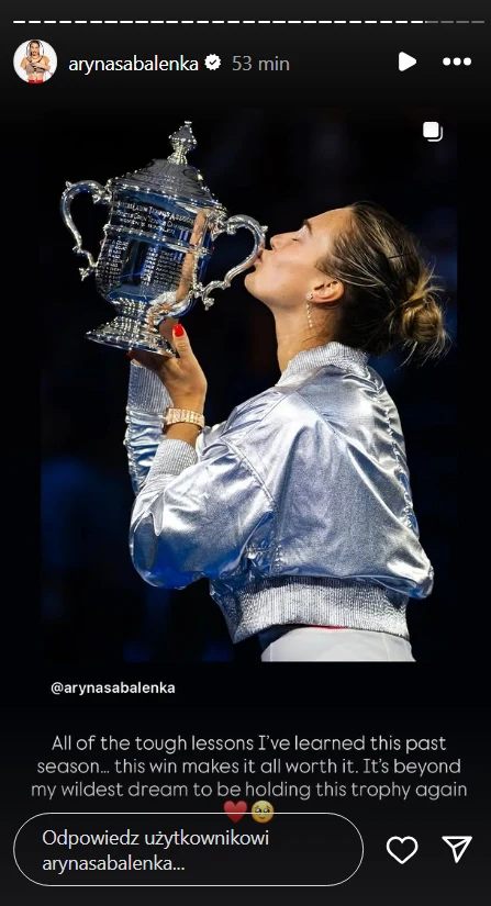 Zawodniczka w srebrnej kurtce całuje puchar, trzymając go w dłoniach, na tle ciemnego rozmazanego tła sportowej areny, radość i duma widoczne na twarzy.
