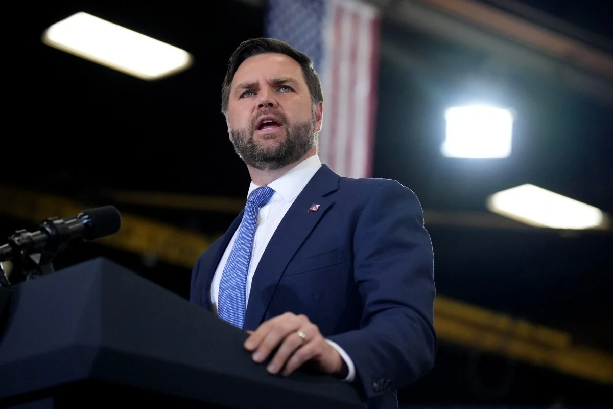 J. D. Vance zabrał głos w sprawie potencjalnego ubiegania się o urząd prezydenta w 2028 r. Mężczyzna w garniturze przemawia przy mównicy, w tle rozmazana flaga Stanów Zjednoczonych i jasne oświetlenie.