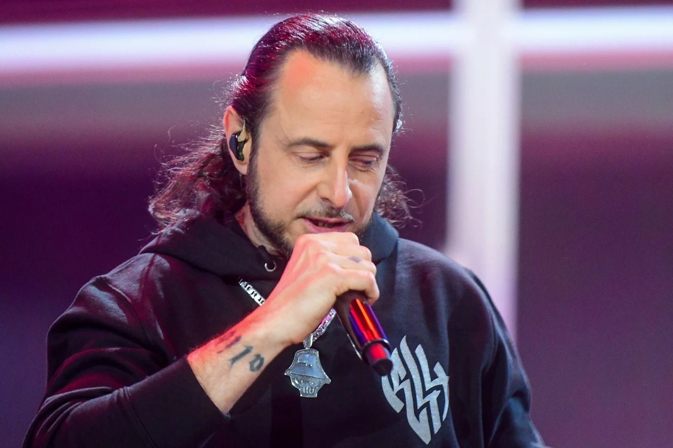 Abradab ogłosił wyjątkowy koncert w hołdzie swojemu bratu Mężczyzna z długimi, ciemnymi włosami trzyma mikrofon i śpiewa, ubrany w czarną bluzę z charakterystycznym białym znakiem graficznym na piersi, na szyi wisi medalion.