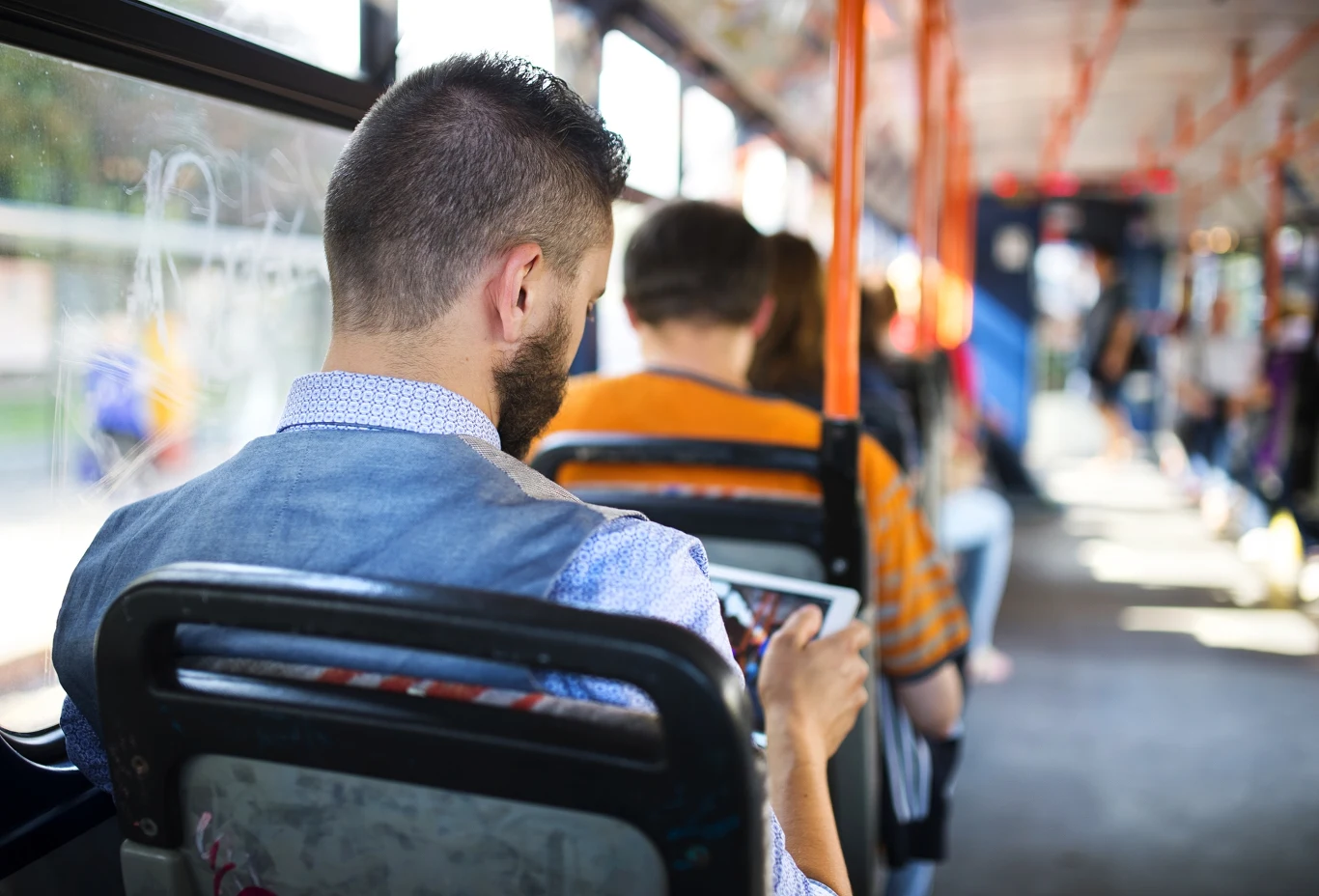 W niektórych miastach Polski komunikacja jest całkowicie bezpłatna Mężczyzna z brodą siedzi w autobusie, patrzy na swój tablet, wokół inni pasażerowie zajęci własnymi sprawami, światło wpada przez okna pojazdu.