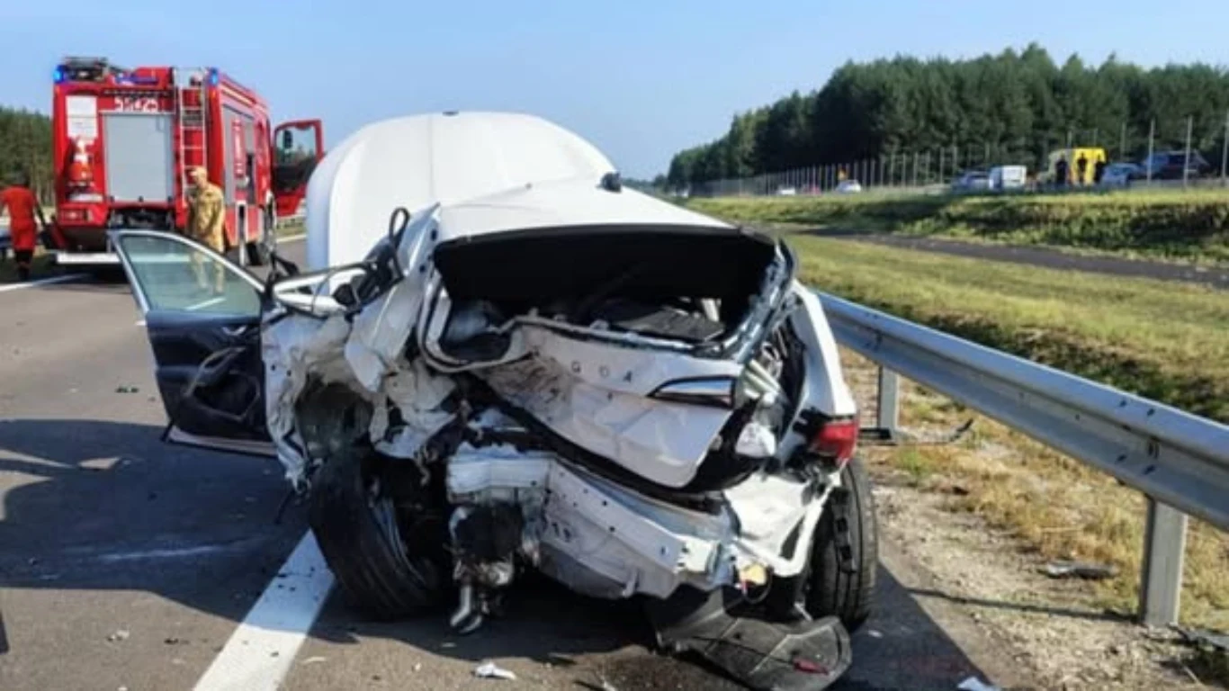 Prokuratura wszczęła śledztwo ws. wypadku, w którym zginęła dziennikarka Rozbity biały samochód na poboczu autostrady z widocznymi poważnymi uszkodzeniami tyłu pojazdu, otwartymi drzwiami kierowcy, w tle zaparkowany wóz strażacki oraz służby ratunkowe, asfaltowa droga, metalowe barierki i pas zieleni