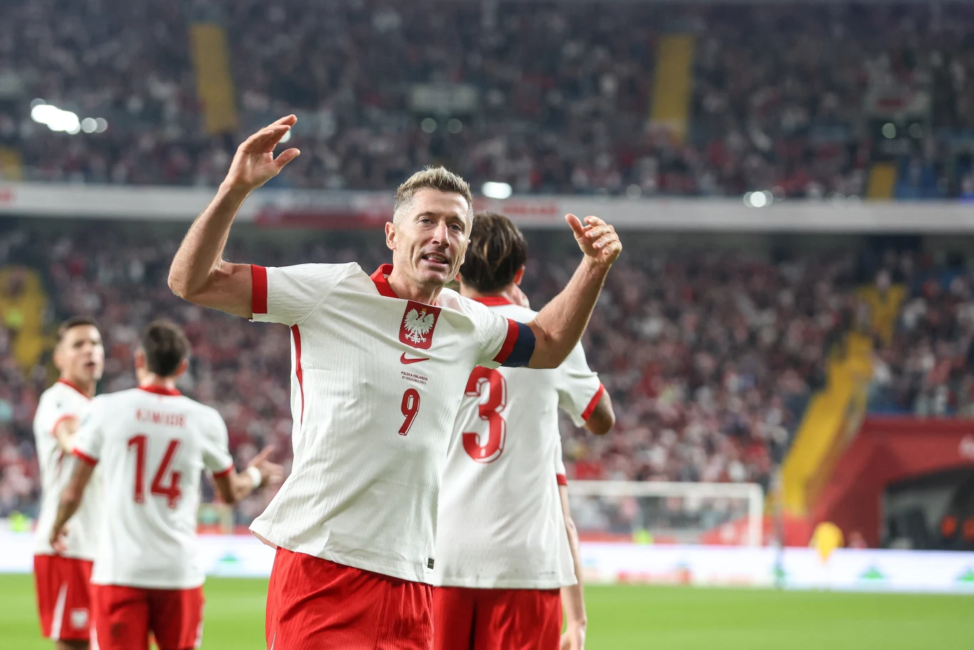Robert Lewandowski Piłkarze reprezentacji Polski w biało-czerwonych strojach świętują zdobycie bramki na stadionie, tłum kibiców w tle oraz piłkarz z numerem 9 na pierwszym planie unoszący ręce w geście radości.