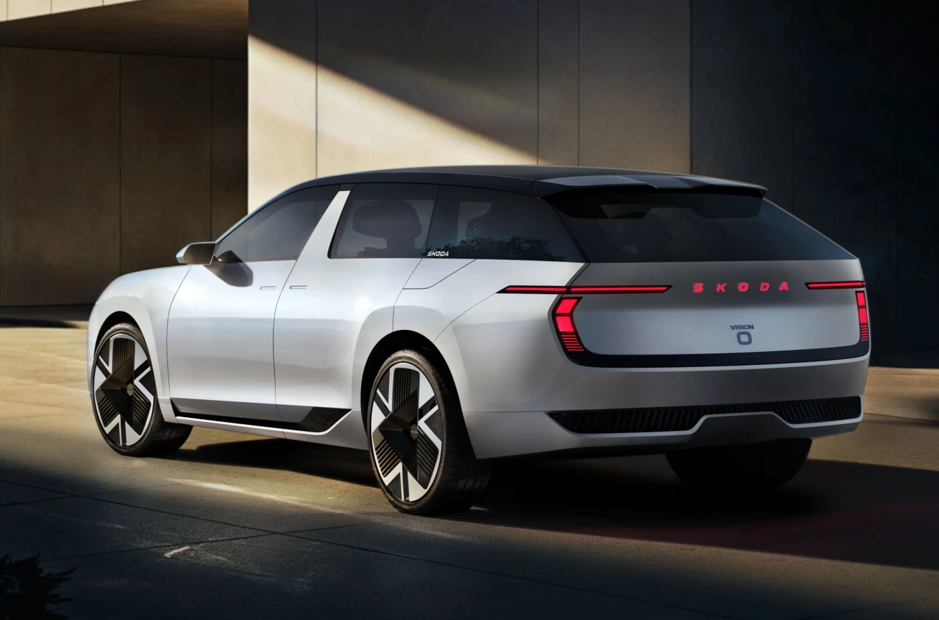 Nowoczesny samochód koncepcyjny marki Škoda o futurystycznym designie, wyrazistych liniach i charakterystycznych światłach LED z tyłu, zaparkowany w pobliżu nowoczesnego budynku, z dużymi felgami i aerodynamicznym nadwoziem.