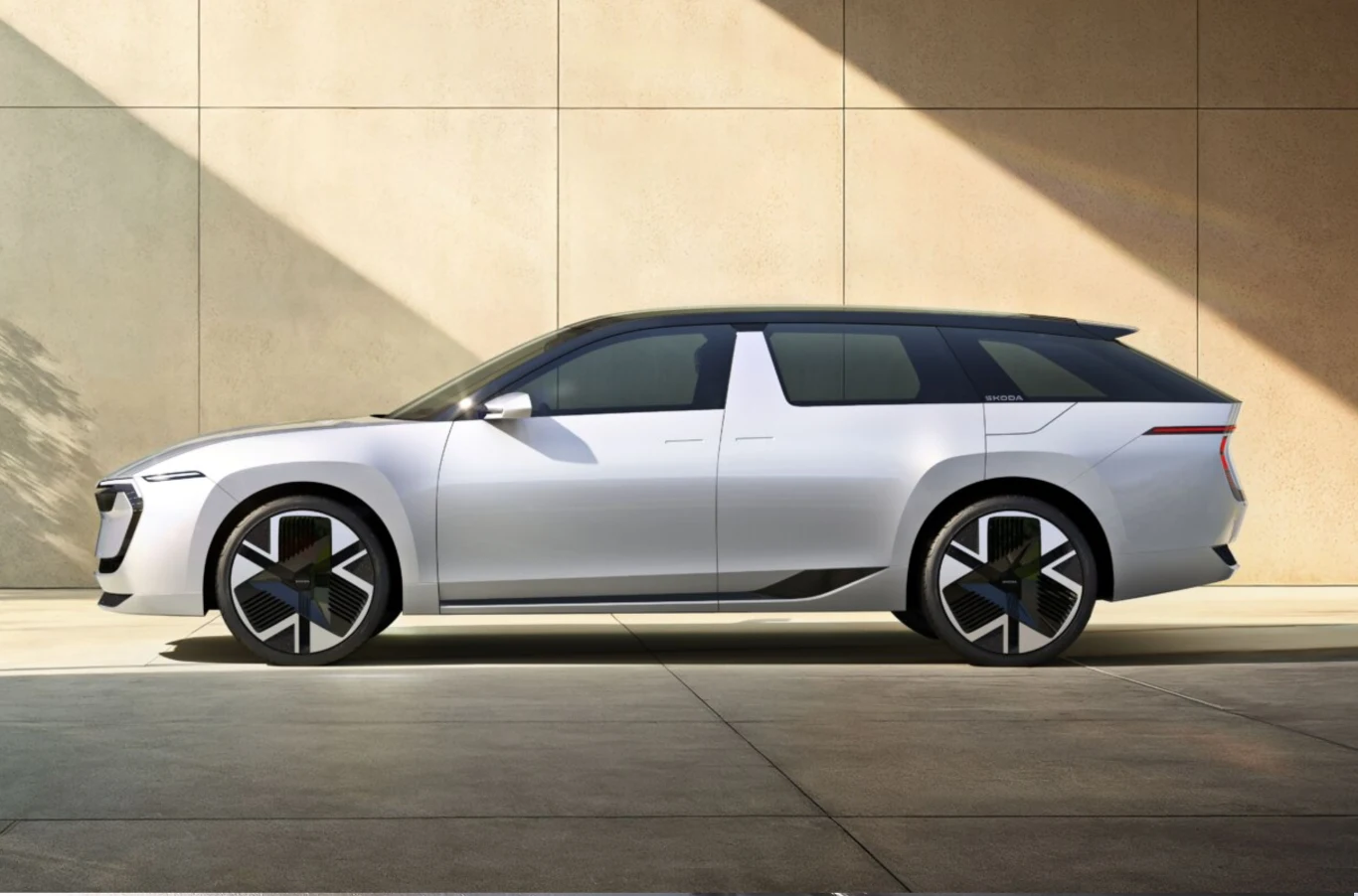 Nowoczesny, futurystyczny samochód typu SUV w jasnym kolorze ustawiony bokiem na tle minimalistycznej ściany, auto ma designerskie felgi i przeszklony dach.