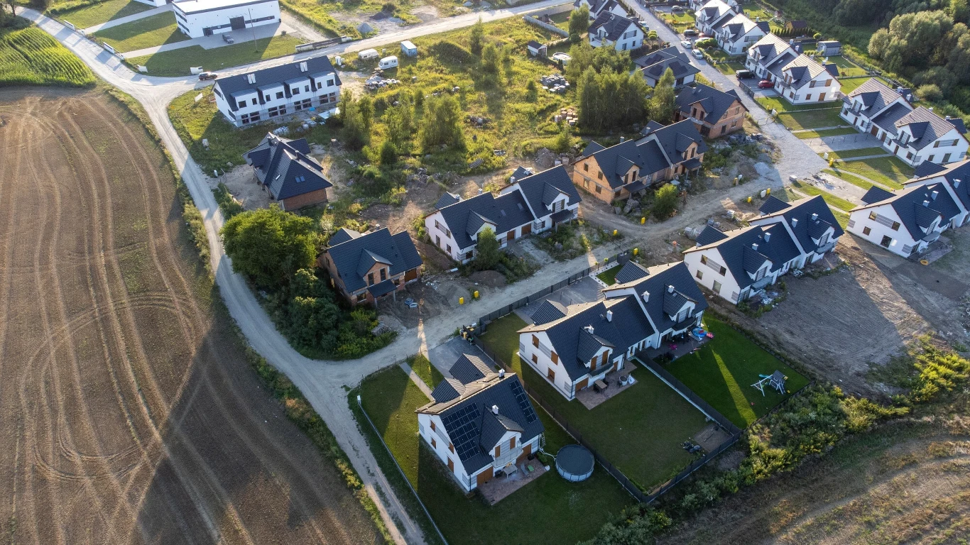 Planowanie przestrzenne po nowemu. Gminy biją na alarm (zdj. ilustracyjne) Nowoczesne osiedle domów jednorodzinnych otoczone polami uprawnymi, uporządkowane ulice, zielone ogrody i nowe budynki w trakcie budowy.