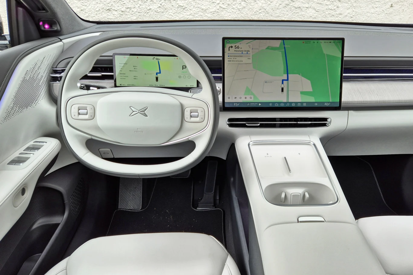 Nowy Xpeng G6 otrzymał między innymi zmienioną kierownicę oraz kratki nawiewów z manualnym sterowaniem Minimalistyczne i nowoczesne wnętrze samochodu z jasną tapicerką, cyfrową deską rozdzielczą oraz dużym ekranem centralnym wyświetlającym mapę nawigacji, elegancka kierownica z logo producenta.