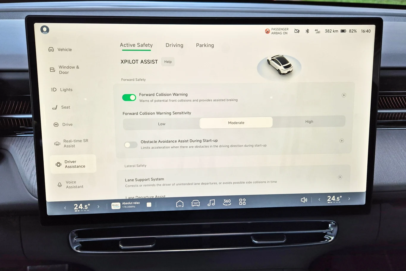 Centralny ekran o przekątnej 15,6 cala ma przejrzyście rozplanowane menu, ale z uwagi na liczbę dostępnych opcji, łatwo się tu pogubić Panel dotykowy systemu multimedialnego samochodu prezentuje sekcję aktywnego bezpieczeństwa, menu ustawień asystentów jazdy oraz parametry takie jak ostrzeżenie o kolizji i czułość systemów bezpieczeństwa, wyświetlając kluczowe funkcje i temperaturę na...
