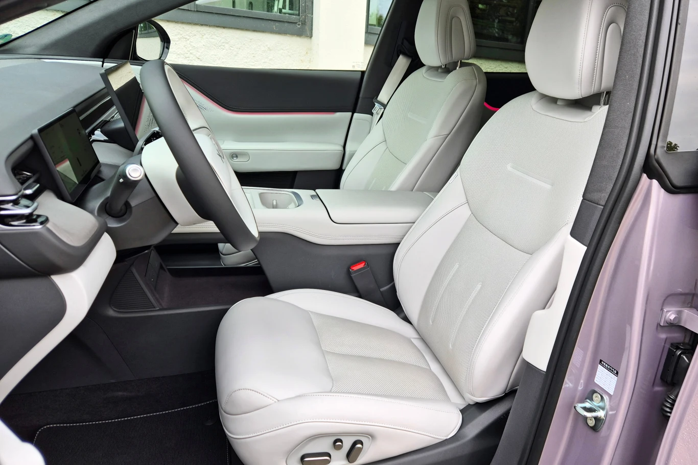 Fotele w Xpengu G6 są całkiem wygodne, ale słabo trzymają na zakrętach. Miła w dotyku skórzana tapicerka jest seryjna, podobnie jak elektryczna regulacja, podgrzewanie, wentylacja oraz masaż Nowoczesne wnętrze samochodu z jasną tapicerką, komfortowe fotele regulowane elektrycznie, konsola środkowa z eleganckim panelem sterowania oraz obszerne drzwi po stronie pasażera, wyraźnie zaprojektowany kokpit z ekranem dotykowym.