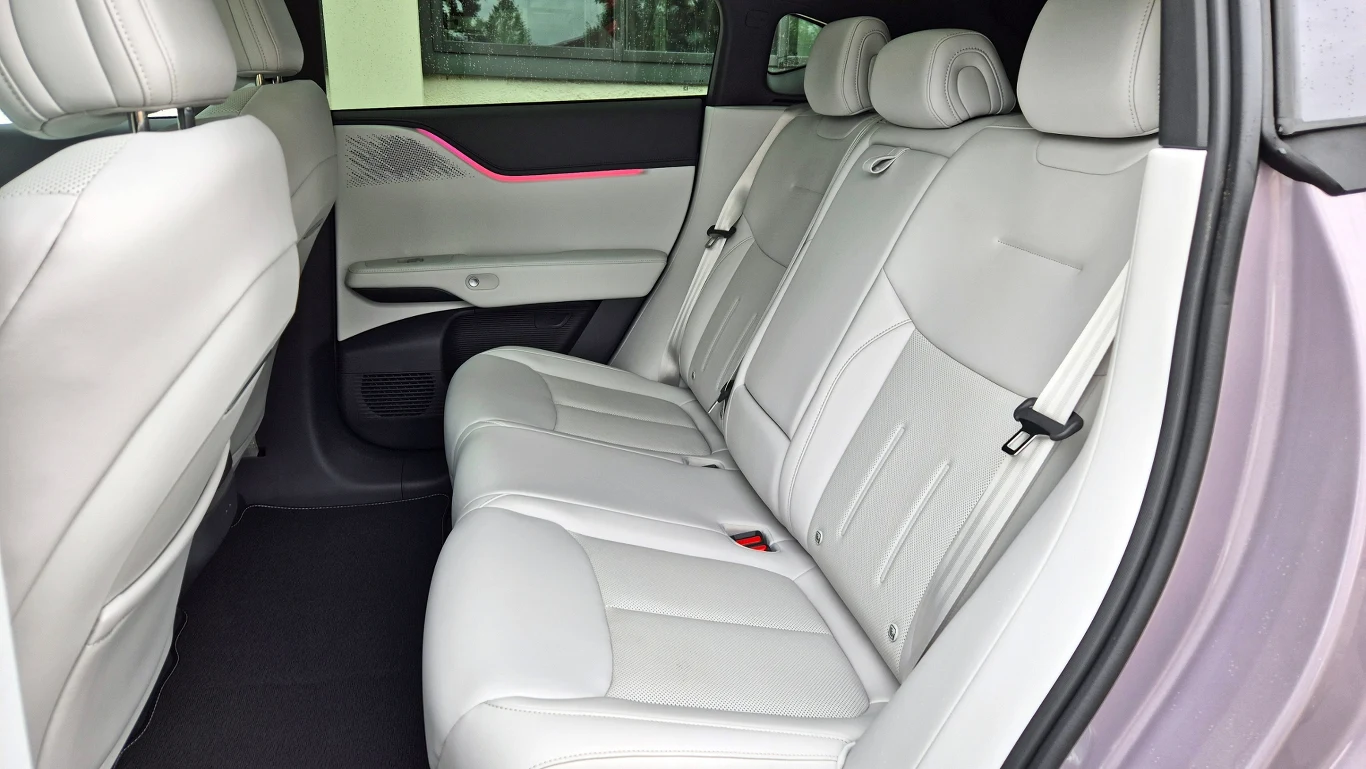 Xpeng G6 ma sylwetkę w stylu coupe, a mimo to miejsca na tylnej kanapie jest całe mnóstwo - również nad głowami podróżnych Tylny rząd jasnych, skórzanych siedzeń samochodu z trzema zagłówkami oraz czarną podłogą, widoczna elegancka tapicerka i dekoracyjne elementy drzwi.