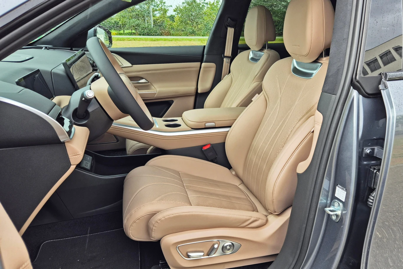 Xpeng G9 ma bardzo dobre fotele wykończone naturalną skórą Kokpit samochodu z beżowymi, skórzanymi fotelami, kierownicą oraz deską rozdzielczą, widoczne elementy nowoczesnego wyposażenia oraz duże przeszklenie drzwi.