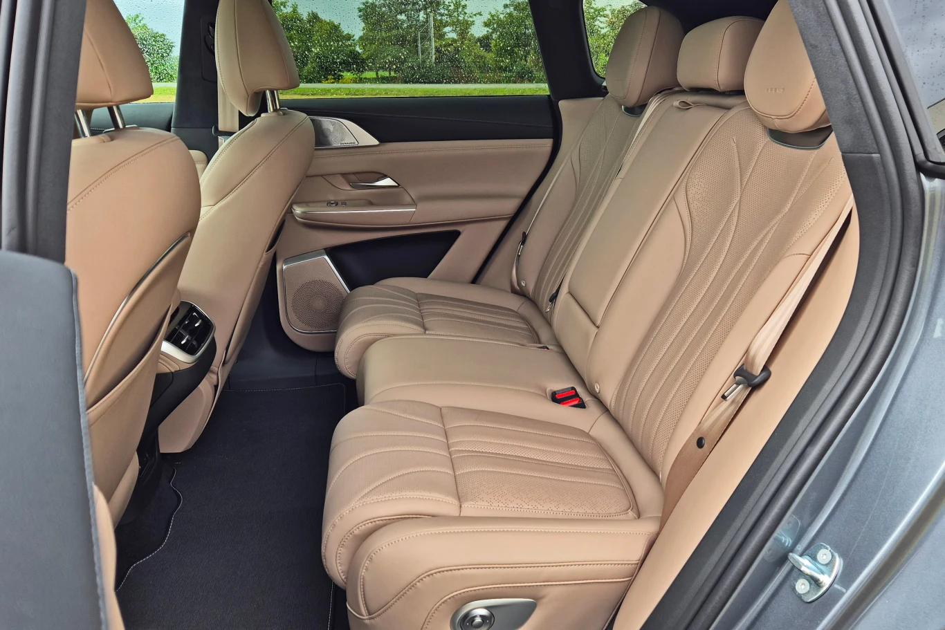 Tylna kanapa Xpenga G9 jest elektrycznie regulowana, a także podgrzewana, wentylowana oraz ma funkcję masażu Beżowe, skórzane siedzenia tylnej kanapy samochodu, przestronne wnętrze, eleganckie wykończenie drzwi, widok na zieleń przez okna.