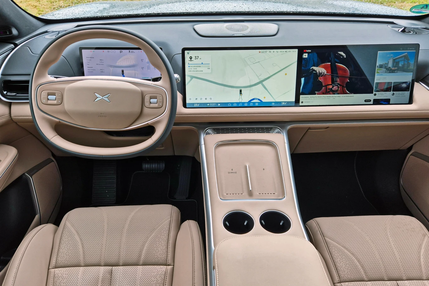 Deska rozdzielcza Xpenga G9 zdominowana jest przez dwa 15-calowe ekrany Nowoczesne wnętrze samochodu elektrycznego z trzema dużymi ekranami na desce rozdzielczej, beżowe skórzane fotele oraz minimalistyczna konsola środkowa z miejscem na napoje.