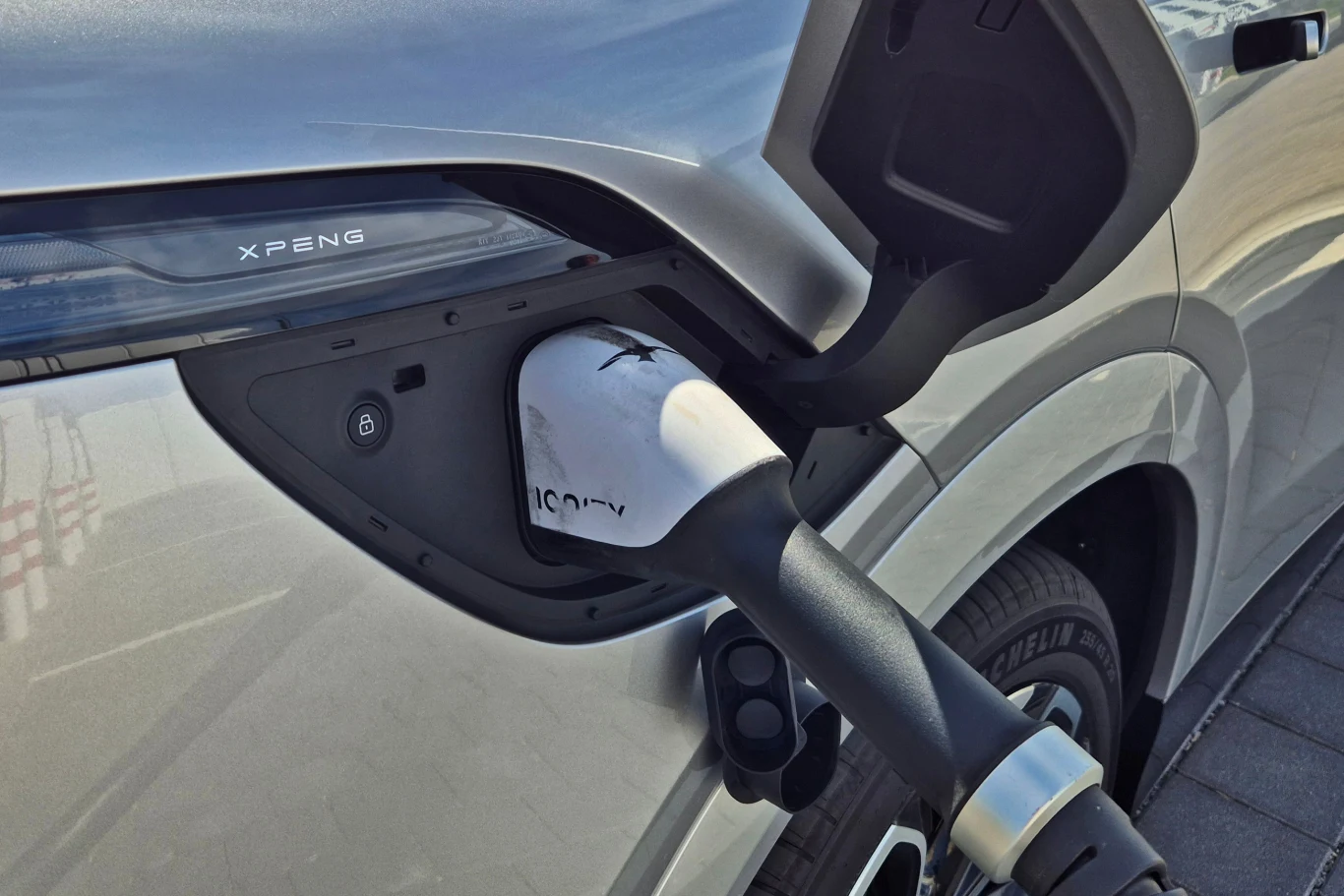 Dzięki nowym bateriom litowo-żelazowo-fosforanowym Xpeng G6 może ładować się z mocą nawet 451 kW Zbliżenie na port ładowania samochodu elektrycznego podczas podłączania kabla ładującego, na karoserii widoczny napis XPeng.