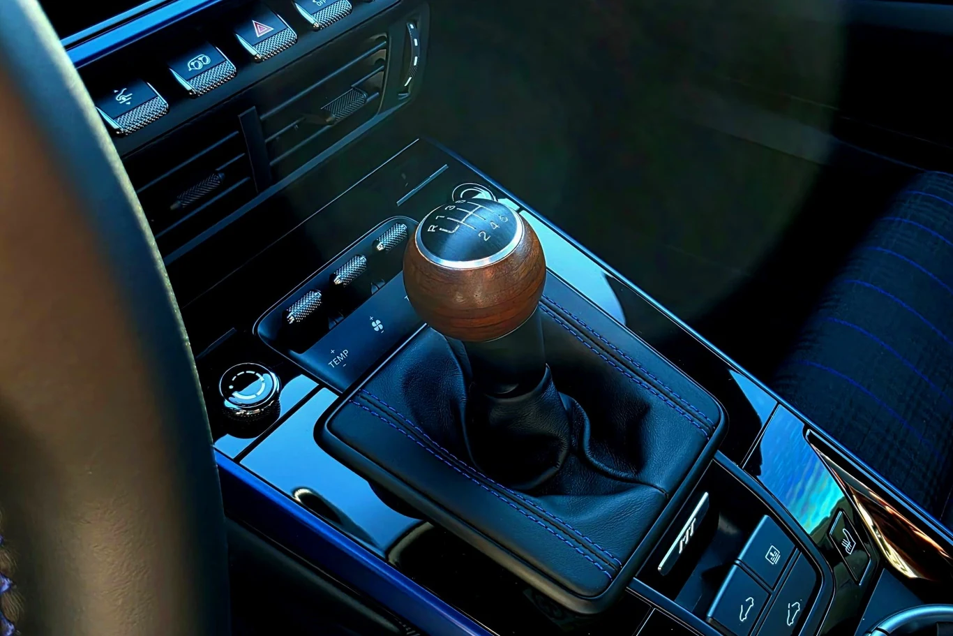 Ręczna skrzynia biegów z gałką zmiany biegów o drewnianym wykończeniu otoczona czarnymi elementami konsoli środkowej nowoczesnego samochodu.