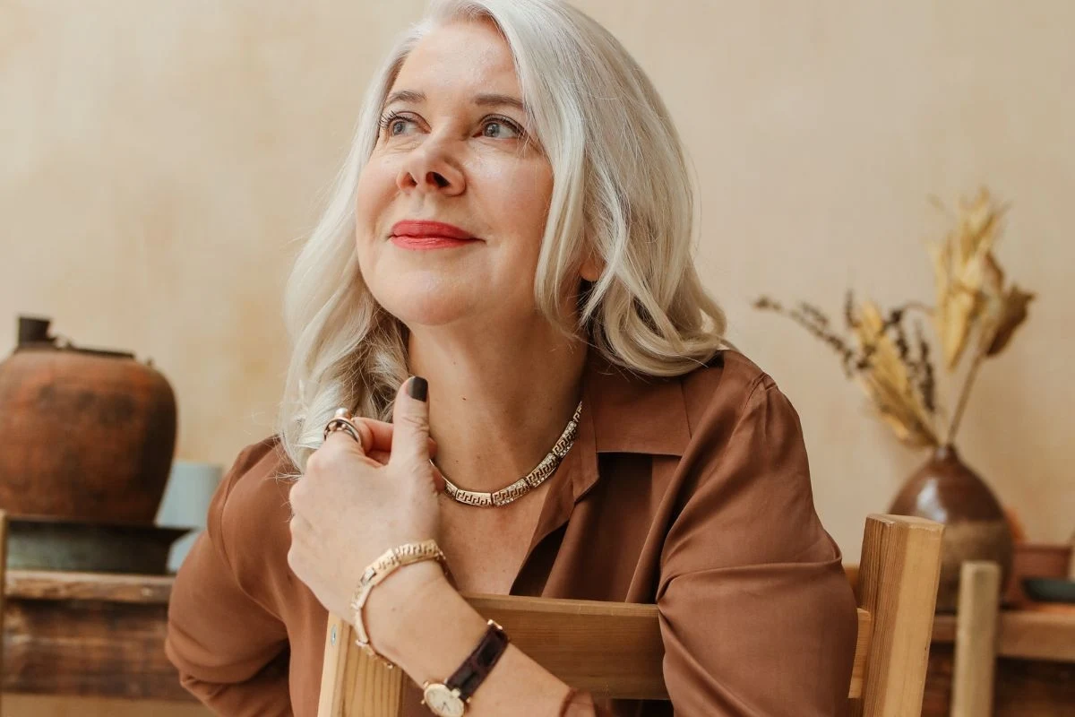 Po 10 września zmienią przyszłość trzech znaków zodiaku. Jesteś na liście? Starsza kobieta o siwych włosach siedzi przy stole, ubrana w brązową koszulę, z dyskretną biżuterią na ręku i szyi, patrzy z uśmiechem w górę; w tle ceramiczne naczynie i dekoracja z suszonych traw.