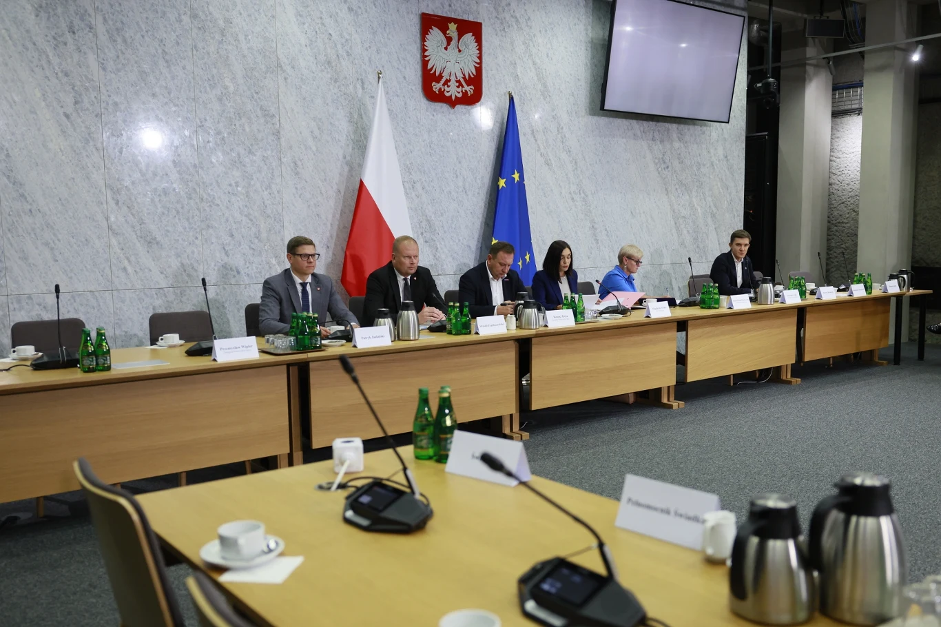 Krystian Dobrzyński nie stawił się przed komisją śledczą Sześć osób siedzących przy długim stole konferencyjnym, na tle godła Polski oraz flag Polski i Unii Europejskiej, w sali z marmurową ścianą; na stole rozmieszczone butelki wody, mikrofony oraz dokumenty.