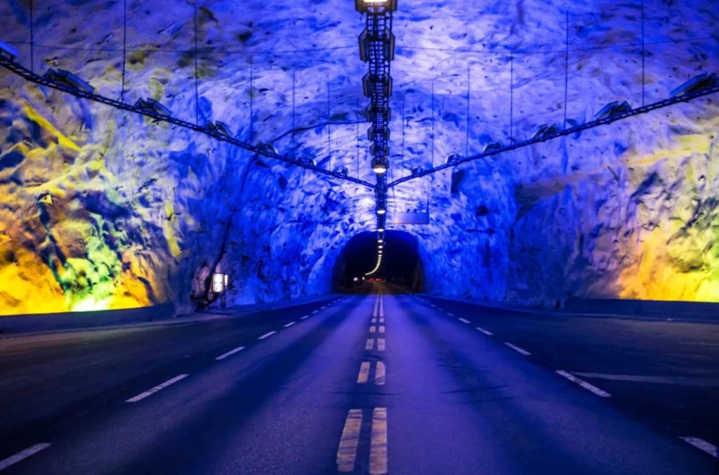 Najdłuższy tunel drogowy świata jest w Norwegii. Ile ma kilometrów? Kolorowo oświetlony tunel drogowy z plastikową nawierzchnią, niebieskie i żółte światła odbijające się od ścian, perspektywa prowadzi w głąb tunelu, a centralny pas drogowy biegnie przez całość.