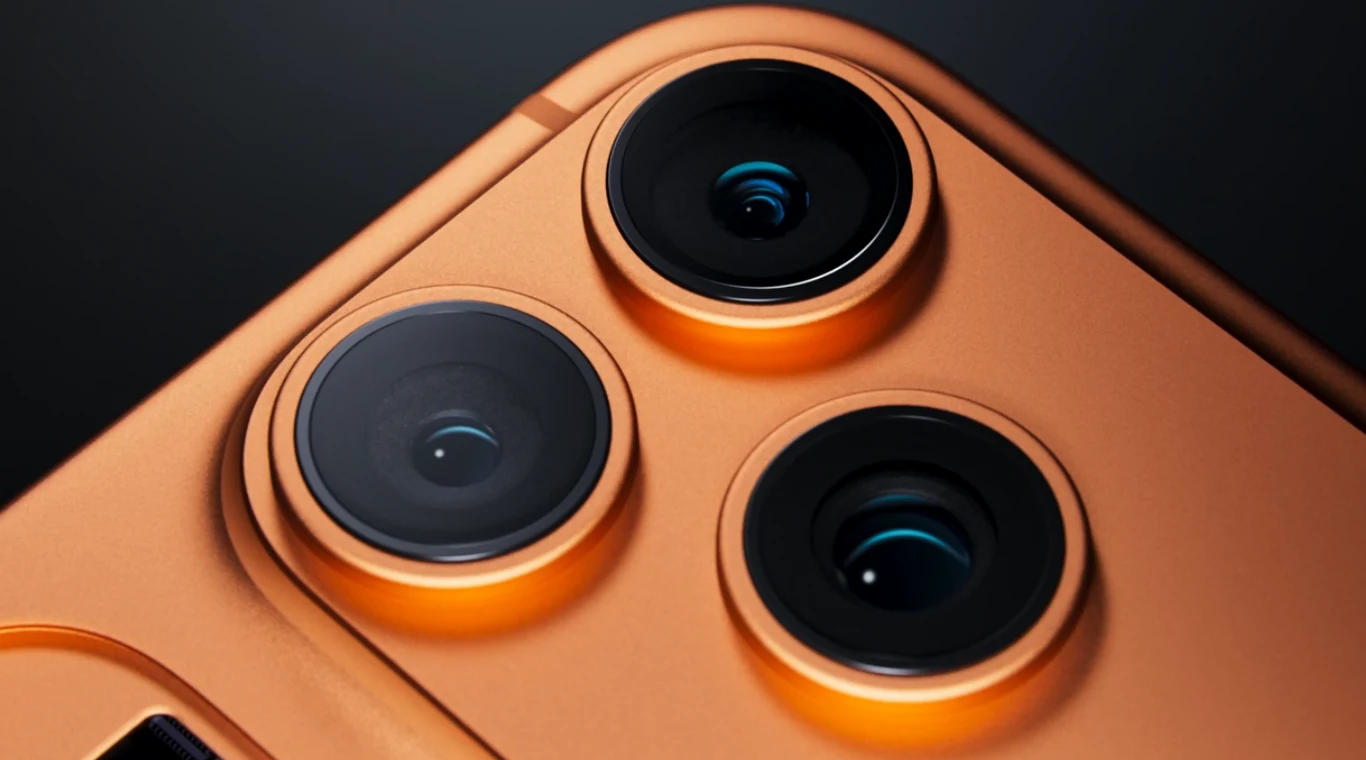 Zbliżenie na trzy obiektywy aparatu fotograficznego zamontowanego w złotej lub pomarańczowej obudowie smartfona, na matowym tle