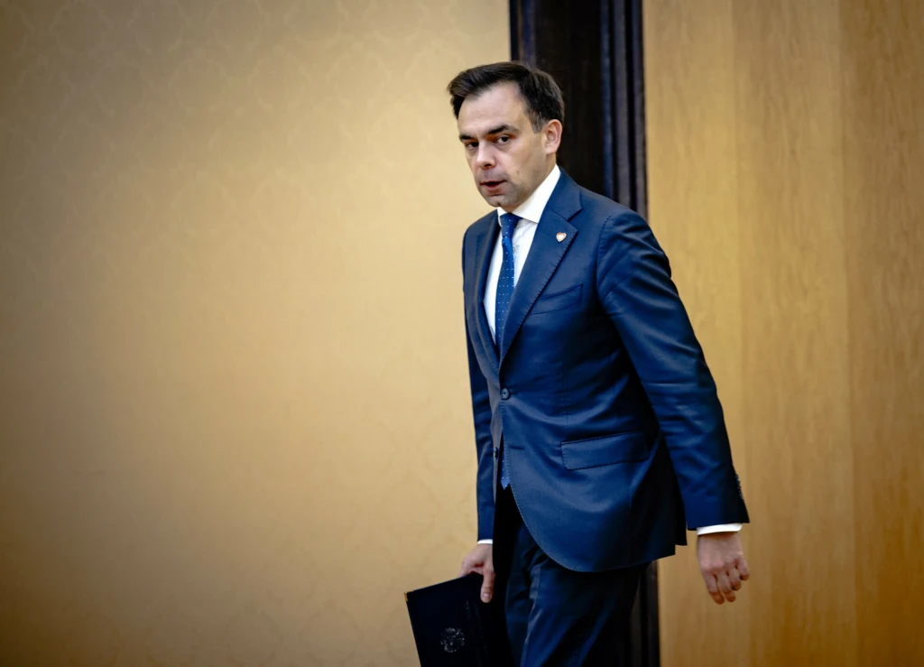 Na zdj. szef MF Andrzej Domański Mężczyzna w granatowym garniturze i białej koszuli z krawatem, trzymający w ręku teczkę, idzie wzdłuż ściany w formalnym wnętrzu.