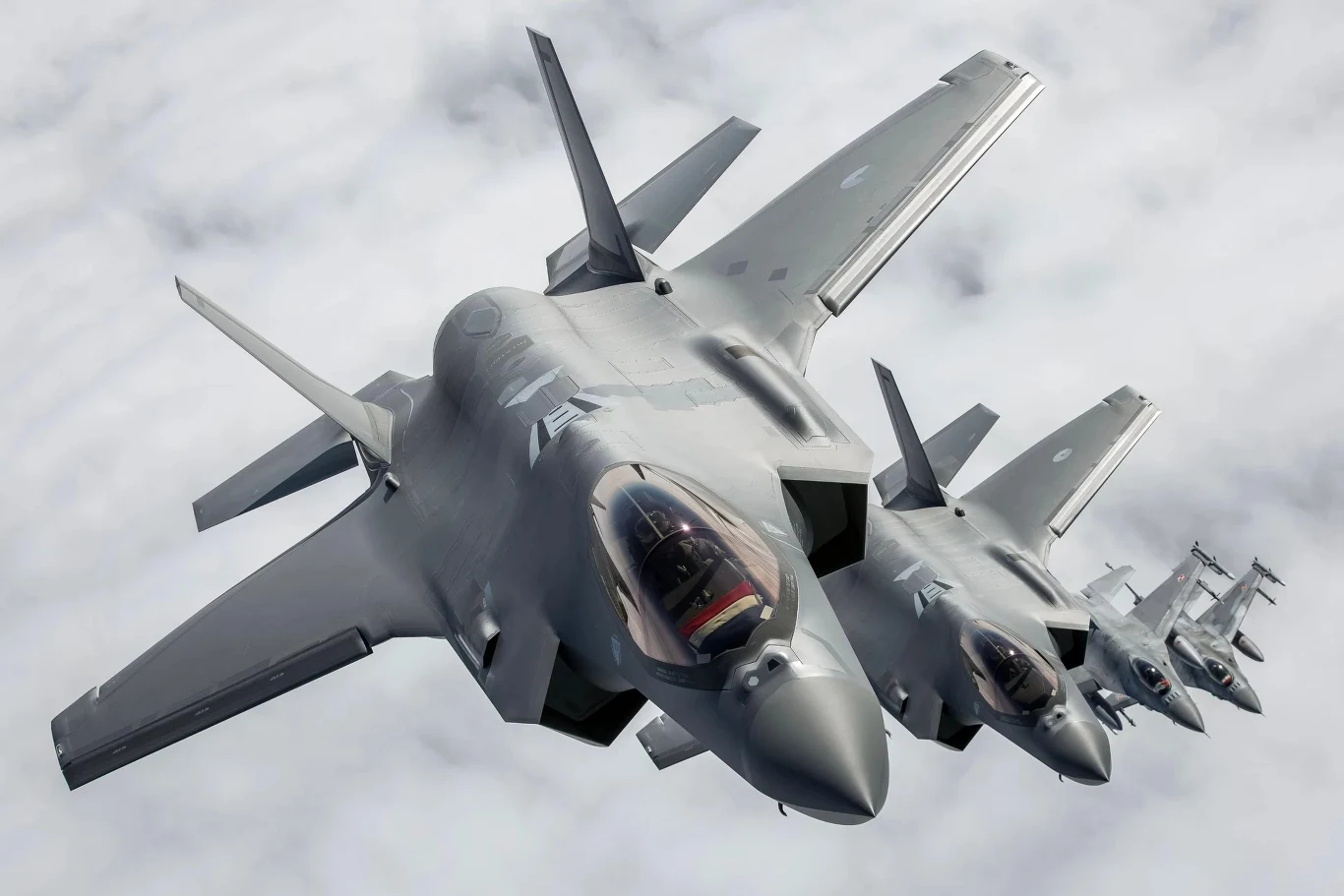 Polskie F-16, holenderskie F-35, włoski G550. Na rosyjskie drony odpowiedziała cała flota NATO Formacja kilku nowoczesnych myśliwców bojowych lecących blisko siebie nad chmurami, wyraźnie ukazane detale kokpitów i aerodynamicznych kształtów samolotów.