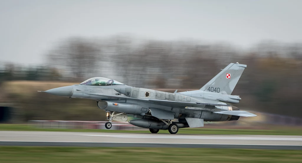 Polski myśliwiec odrzutowy F-16 Myśliwiec F-16 Sił Powietrznych Polski ląduje na pasie startowym podczas dynamicznego manewru, z rozmytym tłem świadczącym o dużej prędkości.
