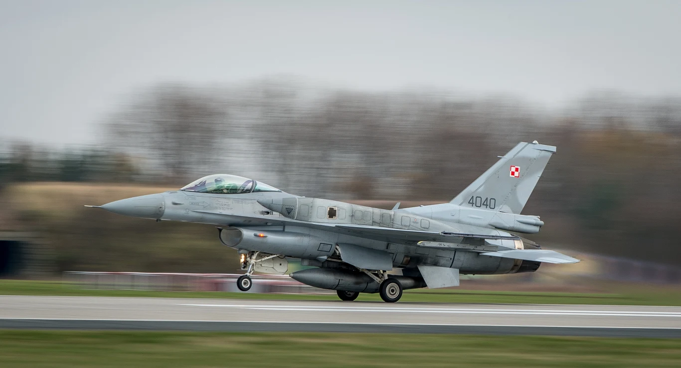 Polski myśliwiec odrzutowy F-16 Myśliwiec F-16 Sił Powietrznych Polski ląduje na pasie startowym podczas dynamicznego manewru, z rozmytym tłem świadczącym o dużej prędkości.