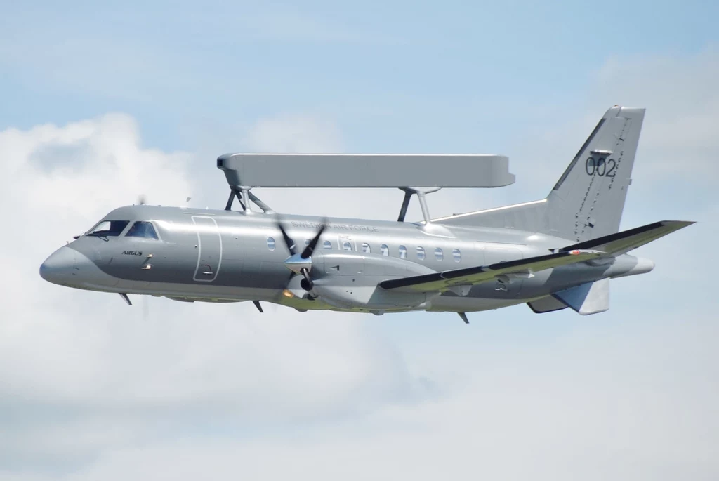 Saab 340 AEW&C Wojskowy samolot rozpoznawczy z dużą anteną radarową zamontowaną nad kadłubem przelatuje na tle nieba.