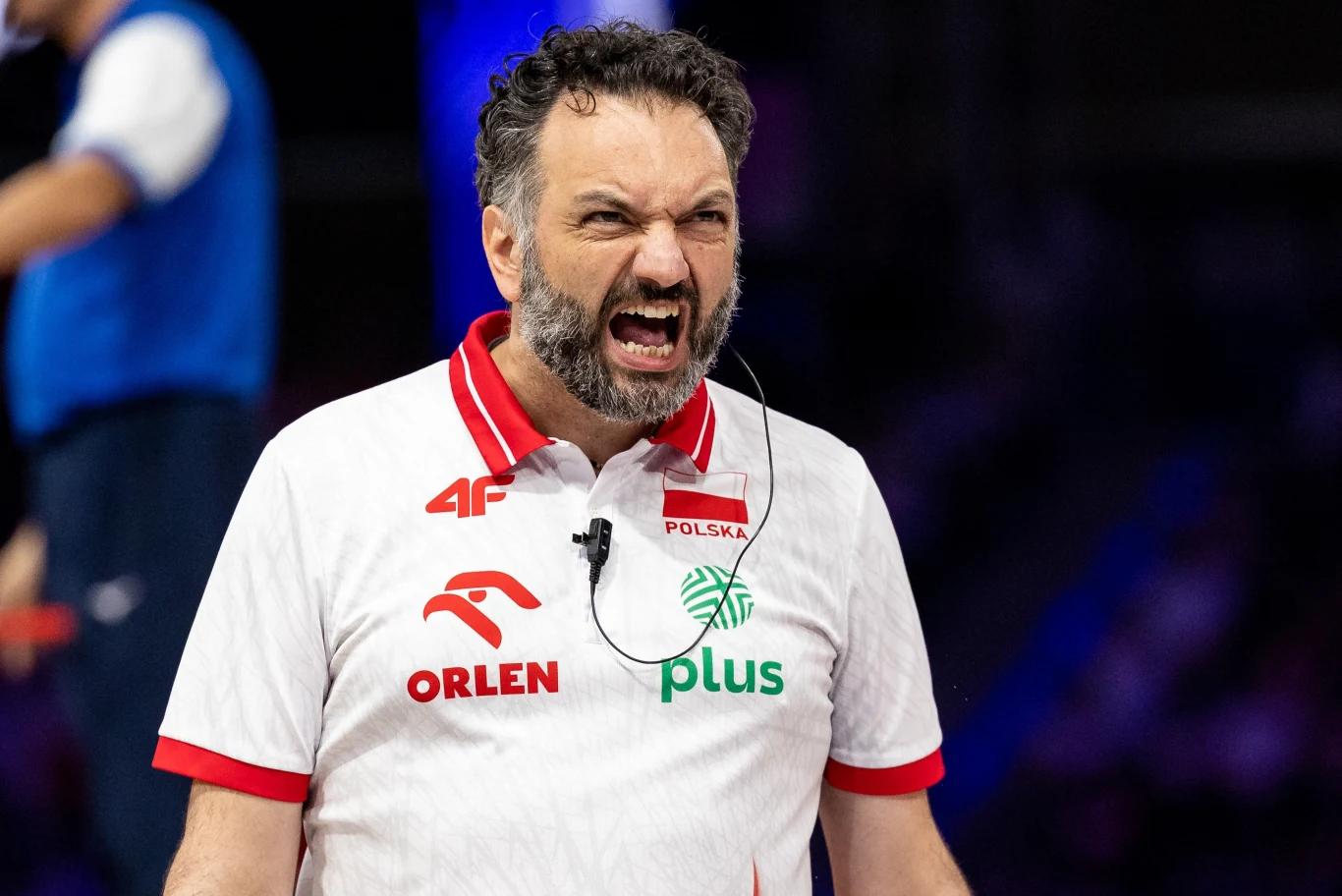 Mężczyzna w białej koszulce z czerwonymi akcentami, z logo ORLEN, Plus i napisem Polska, wyraźnie wyraża emocje, prawdopodobnie podczas wydarzenia sportowego.