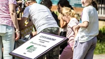 Grupa młodych osób zgromadzonych na zewnątrz podczas akcji ekologicznej, na pierwszym planie tablica informacyjna z napisem 'Czyste Darłowo' i logotypem inicjatywy czystości.
