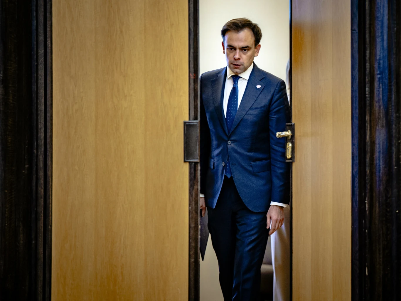 Dług publiczny Polski rośnie. W II kwartale przekroczył 1,76 bln zł (zdj. ilustracyjne) Mężczyzna w garniturze i krawacie wychodzi przez częściowo otwarte, drewniane drzwi, jego wyraz twarzy jest poważny, w tle widoczne ściany wnętrza budynku.