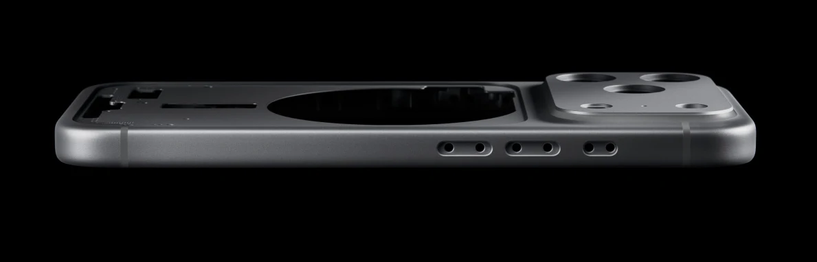 Metalowa ramka telefonu z wycięciami na komponenty i wyeksponowanym miejscem na aparat fotograficzny, widoczna w profilu na czarnym tle.