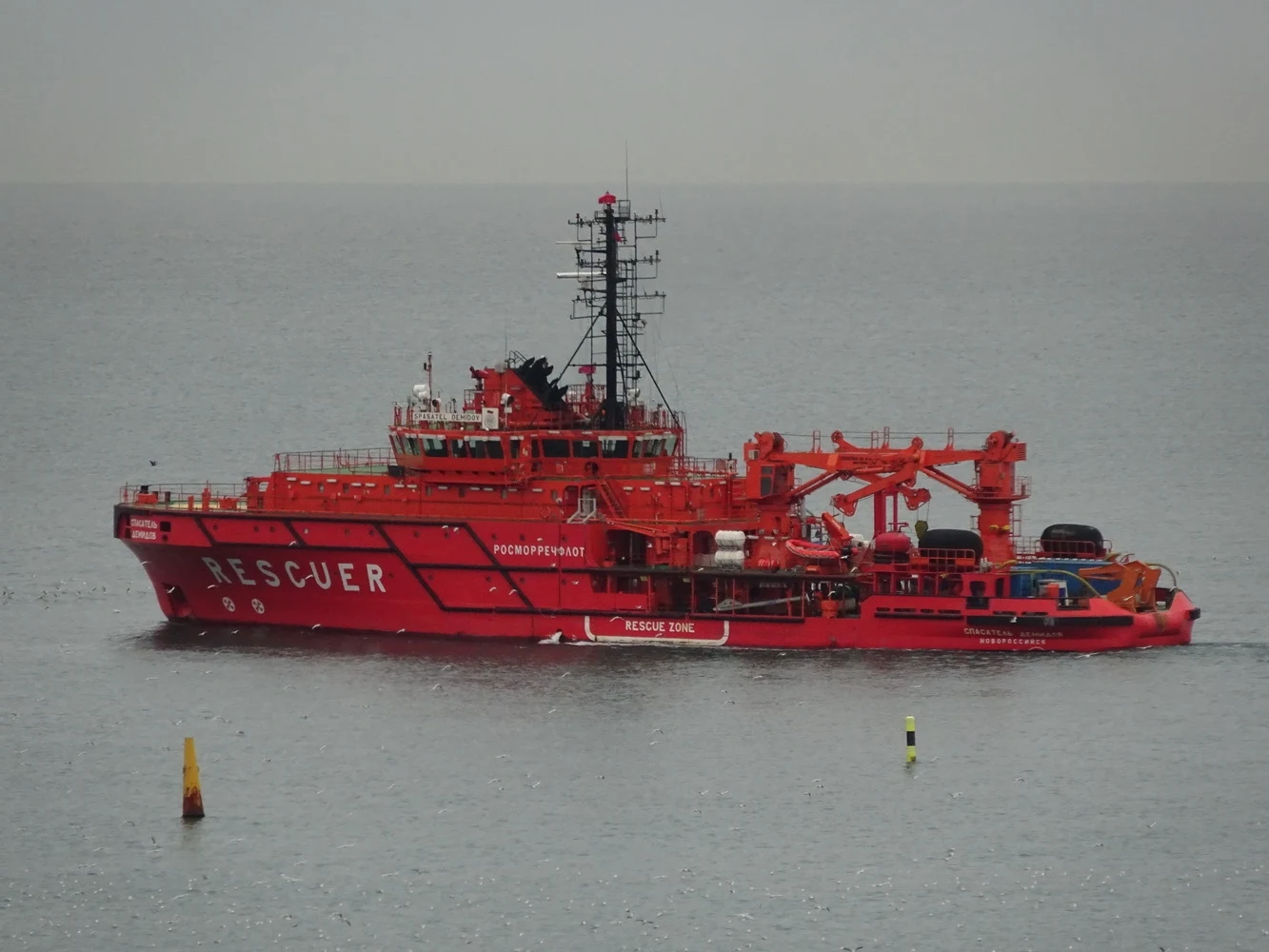 Czerwony statek ratowniczy wyposażony w specjalistyczny sprzęt, płynący po spokojnej wodzie, z widocznym napisem RESCUER na burcie.