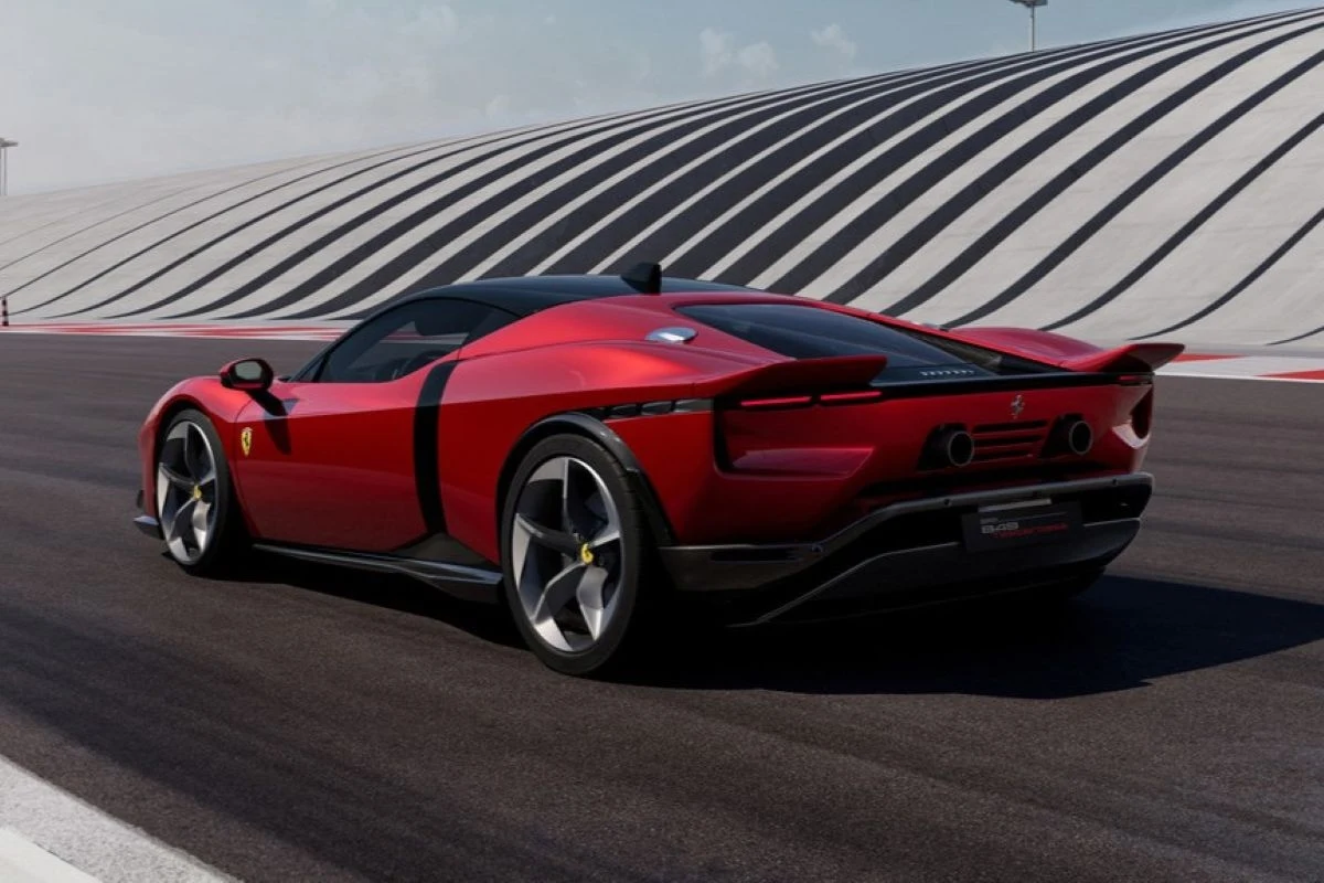 Czerwony, sportowy samochód marki Ferrari porusza się po torze wyścigowym, w tle widoczna jest nowoczesna, pofalowana architektura trybun, całość utrzymana w dynamicznej i eleganckiej stylistyce.