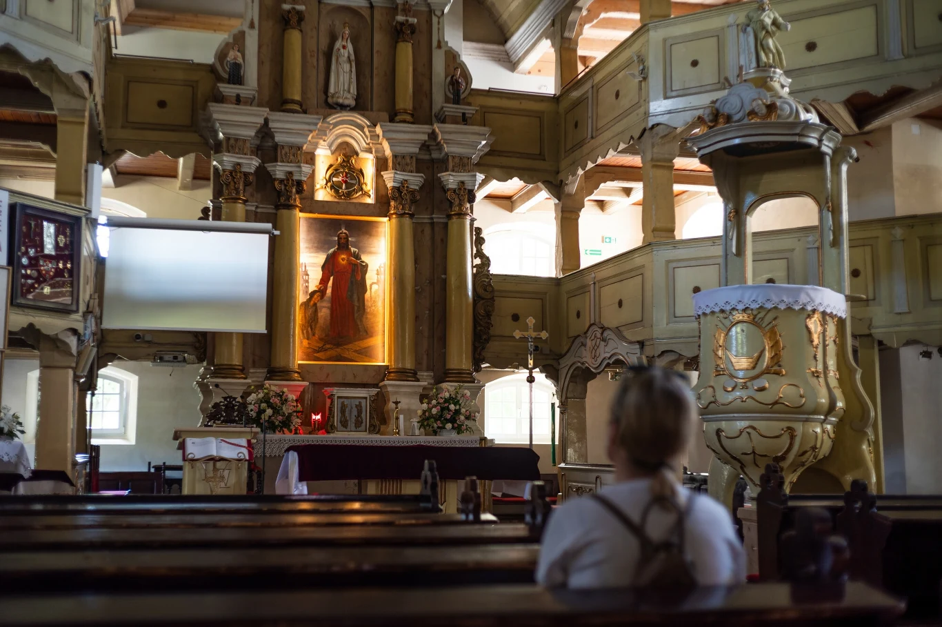 Kim był św. Jan Damasceński? Wnętrze zabytkowego kościoła z drewnianymi balustradami i bogato zdobionym ołtarzem podświetlonym złotym światłem, na pierwszym planie osoba siedząca w ławce patrząca w stronę ołtarza.