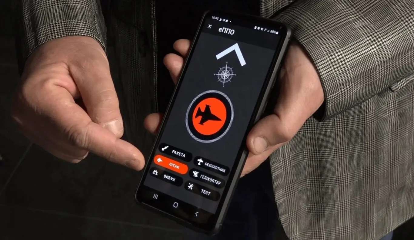 Aplikacja do monitorowania dronów. Powinniśmy brać przykład z Ukraińców. Męska dłoń trzymająca smartfon z aplikacją do rozpoznawania zagrożeń powietrznych, na ekranie widoczny symbol samolotu oraz przyciski oznaczające różne rodzaje obiektów latających.