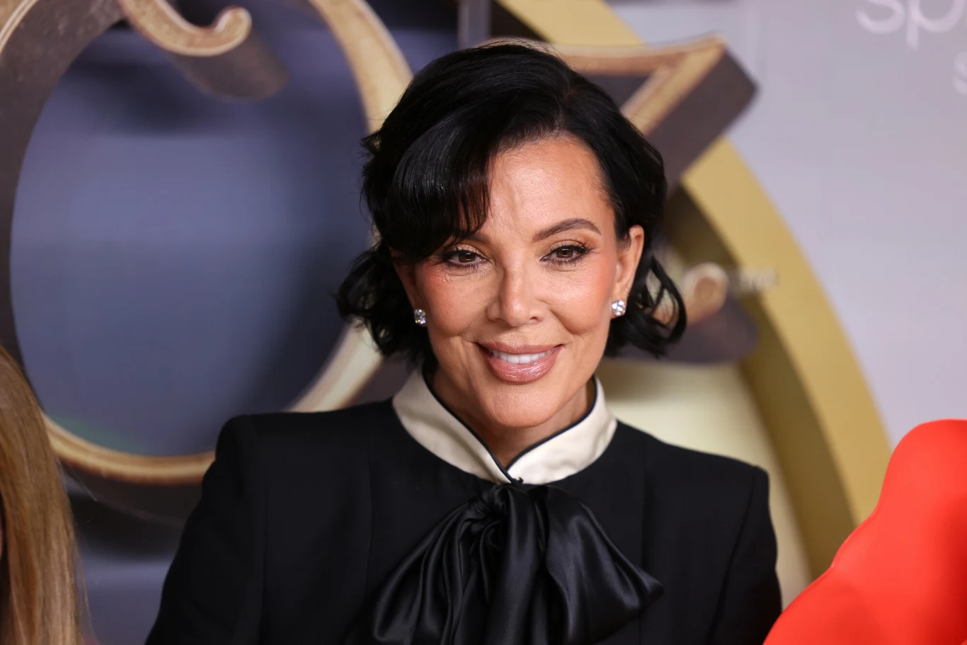 Kris Jenner przeszła lifting za 100 tys. dolarów. Ponoć efekty nie spełniają jej oczekiwań Kris Jenner w eleganckiej czarnej marynarce z białym kołnierzykiem na tle złoto-beżowej dekoracji.