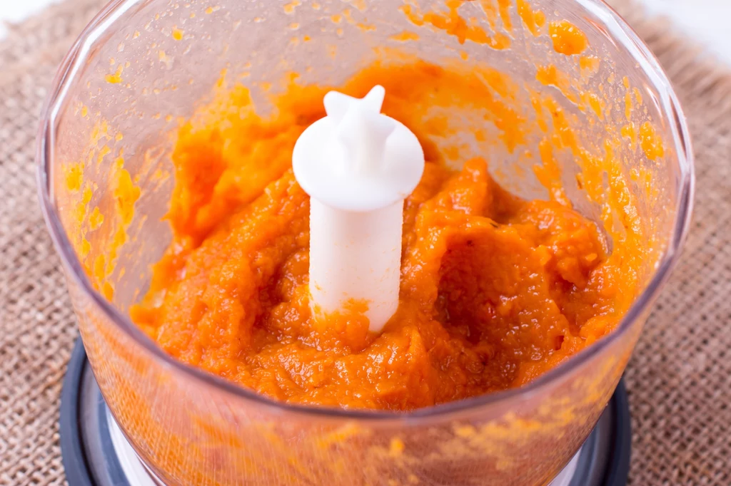 Gęste puree z dyni znajdujące się w szklanym pojemniku blendera, o intensywnie pomarańczowej barwie, z wyraźnym nożem urządzenia pośrodku.