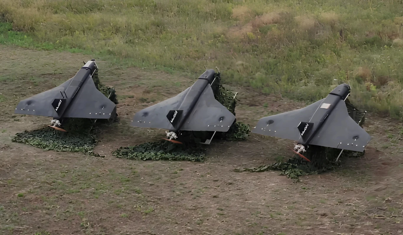 Jak rosyjskie drony dotarły do Polski. Eksperci wskazują szczegóły Trzy bezzałogowe statki powietrzne w kolorze ciemnym ustawione na ziemi w równym rzędzie, na tle trawiastego i nieco pustego terenu
