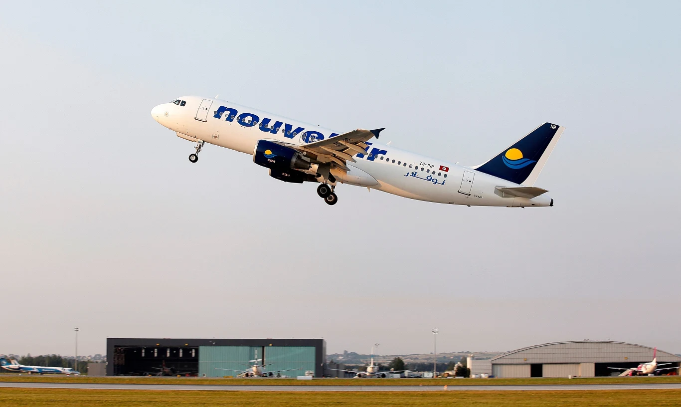 Samolot linii lotniczych Nouvelair lądował awaryjnie w Polsce (zdj. ilustracyjne) Startujący samolot pasażerski linii Nouvelair na pasie startowym lotniska, w tle hangary oraz inne samoloty na płycie lotniska