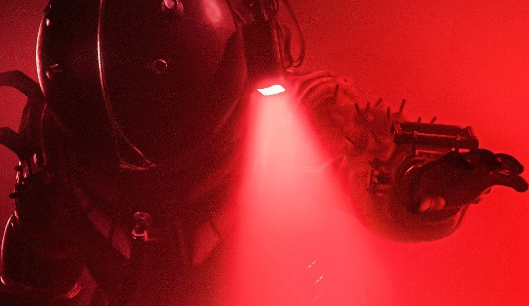 Cronos: The New Dawn Postać w specjalnym kombinezonie ochronnym, oświetlona intensywnym czerwonym światłem, z ręką wyciągniętą do przodu, w otoczeniu gęstej czerwonej mgły.