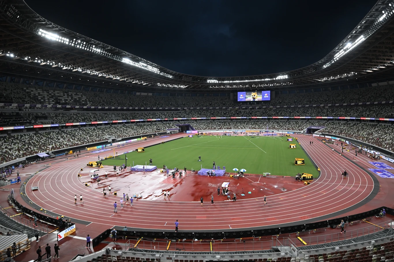 Stadion w Tokio, na którym będą się odbywać lekkoatletyczne MŚ Oświetlony stadion lekkoatletyczny z bieżnią i murawą, otoczony trybunami, na których widoczne są nieliczne osoby; na środku obiektu odbywają się przygotowania do zawodów, a po obu stronach rozłożony jest sprzęt sportowy.