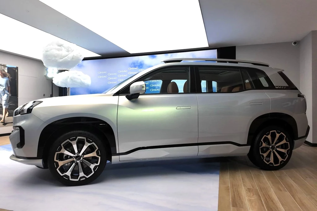 Aion V pod kątem rozmiarów plasuje się w grupie takich elektryków jak Volkswagen ID.4 czy Skoda Enyaq. Srebrny SUV nowoczesnej stylistyki ustawiony na tle jasnego wnętrza ekspozycyjnego z imitacją chmury w tle, podkreślone kształty nadwozia oraz duże, efektowne felgi.